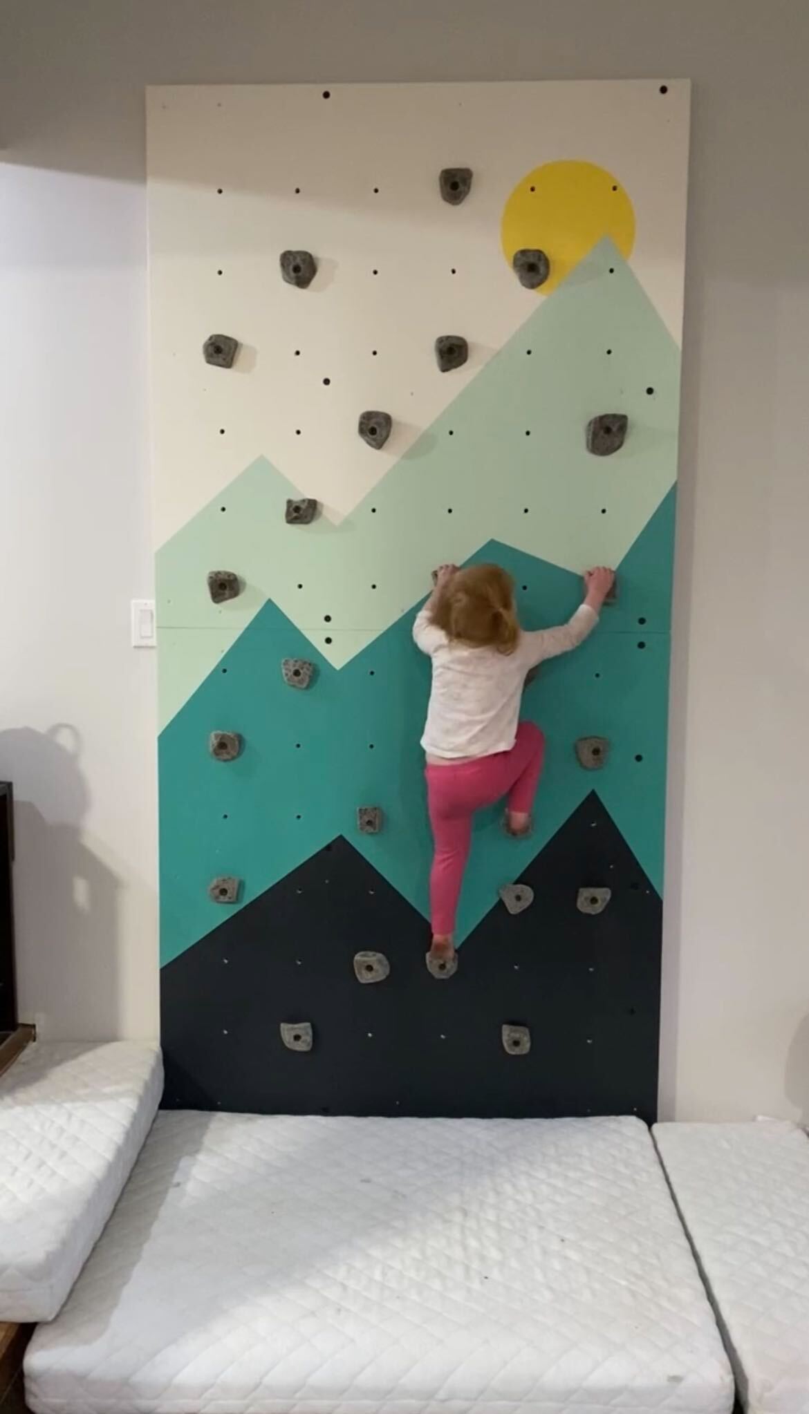 girl climbing kids climbing wall with mountain mural and crash mat